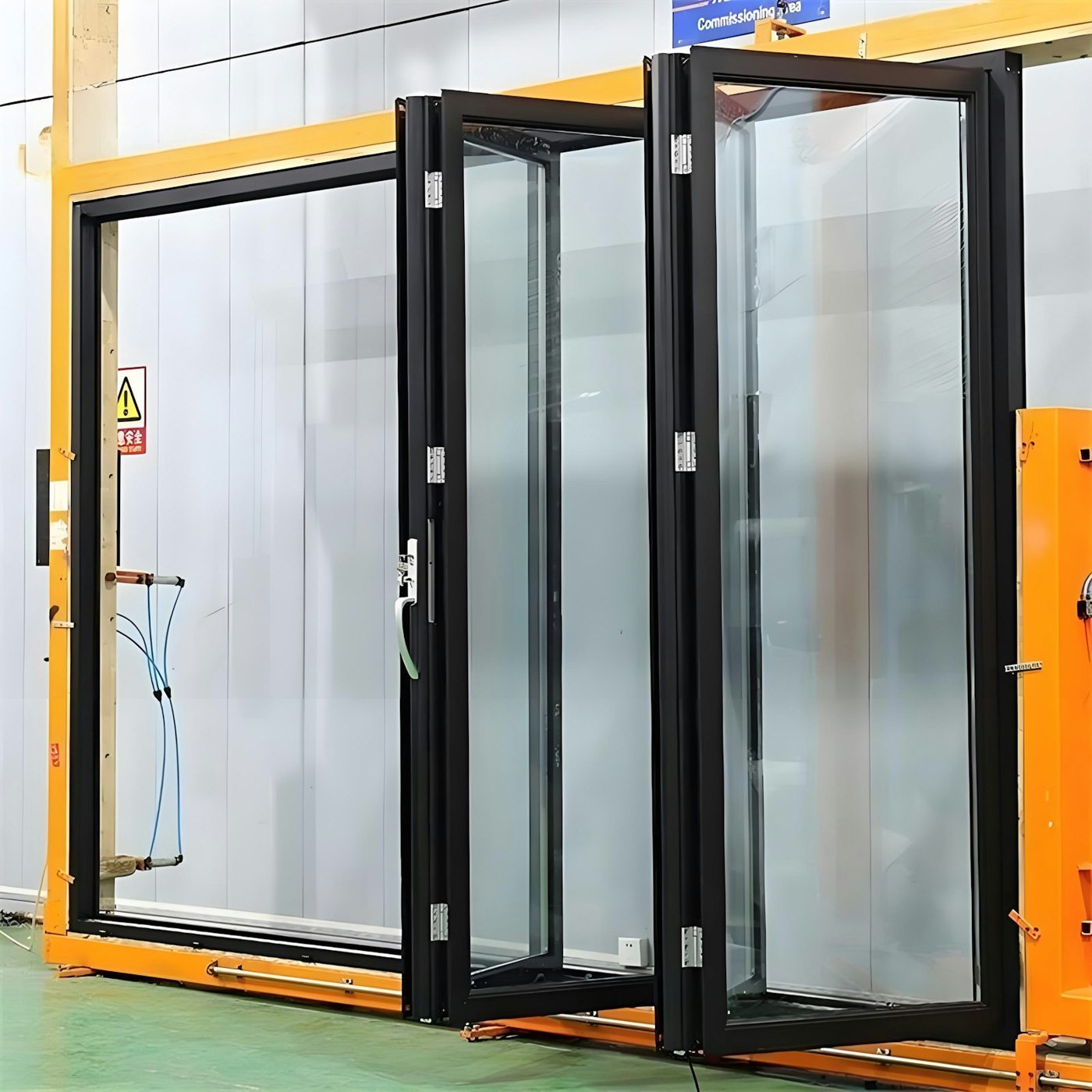 Sistema de hojas acristaladas plegables de marco oscuro en un taller como referencia para puertas de aluminio